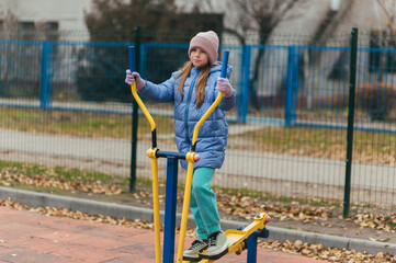 A beautiful, strong teenage girl is engaged in sports and fitness on exercise machines outside at a...
