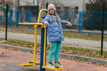 A beautiful, strong teenage girl is engaged in sports and fitness on exercise machines outside at a...
