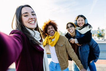 Diverse group of young people having fun taking selfie portrait together outside during winter...