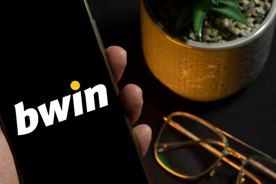 Mobile device displaying Bwin next to a plant and glasses, scene of online sports betting and daily predictions. Bookmaker