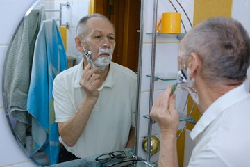 Portrait of an elderly senior man applaying a cream on his face in front of a mirror in bathroom, skincare, beauty and vitality concepts. High quality photo