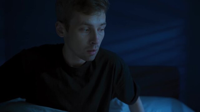 A shocked man abruptly awakes and sits up in bed at night, startled and breathing fast because nightmare disturb his already troubled sleep. Sleep disorder, insomnia and night terror. Space for text