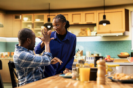 Excited African American couple sharing high five to celebrate good news, working from home together. Man being satisfied with the career opportunity while woman is being supportive.