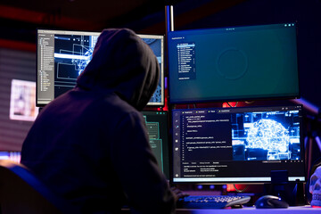 Hooded hacker coding on PC, using AI to evade security with stealth malware. Evil man using artificial intelligence script on computer to hide malicious code from detection systems