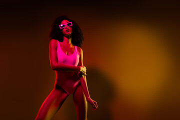 Stylish young woman posing in bright neon lights, wearing a bodysuit, with a colorful illuminated background