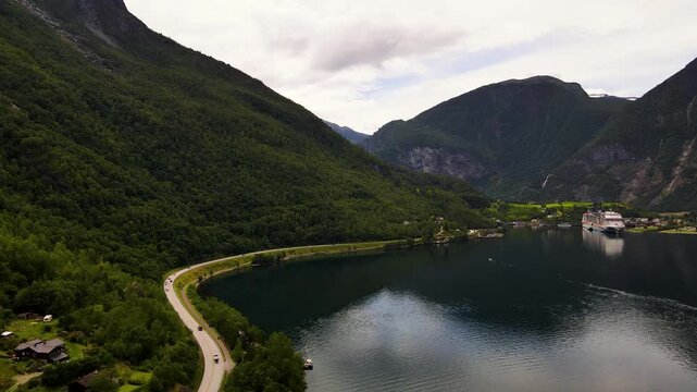 Aerial view of the cruise ship in Flam waters contrasting with the lush green mountains and winding road, creating a stunning landscape, Flam, Vestland, Norway.