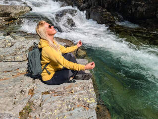 Blonde Woman Meditates by a Rushing Waterfall and Emerald River in the Pristine Norwegian Wilderness, Embracing Nature and Tranquility.