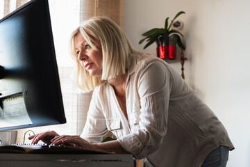 Mature woman standing working at home office desk