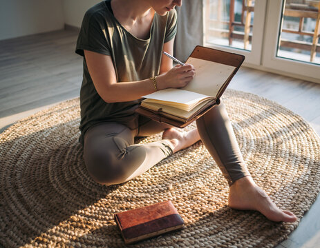 Young woman journaling by lightfilled window. Expressing thoughts, planning goals, or simply reflecting. Promotes wellness, mindfulness, creativity, and lifestyle. - Powered by Adobe