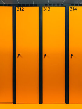 Bright orange gym lockers in a clean, modern sports facility. Minimalistic design with numbered doors creating a bold visual pattern.