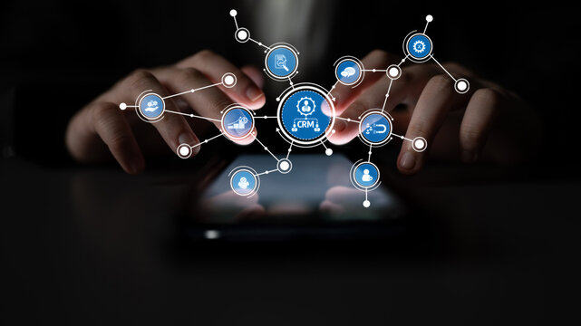 Focused hands engage with a smartphone displaying a network of CRM icons, symbolizing the synergy of technology and customer relations in a contemporary setting. Tessel