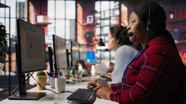 IT support expert at PC in call center office troubleshoots errors to minimize downtime. Tech support agent at desk writing code, maintaining technical systems and infrastructure, camera B