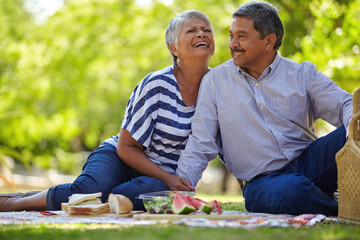 Senior couple, laugh and picnic outdoor with love, romantic date and bonding together. Happy, elderly people and funny joke with food, sightseeing and partner affection of anniversary holiday at park