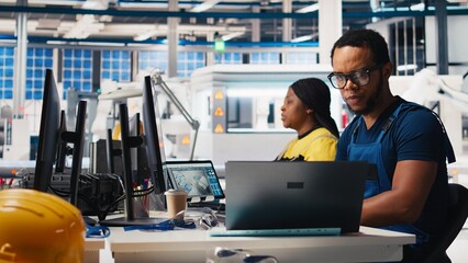 Black engineer inputs solar system parameters at industrial workstation, using PC in a renewable...