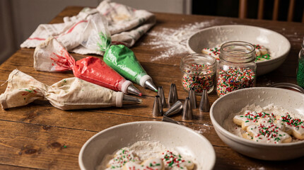 A close-up of holiday cookie decorating tools—piping bags, sprinkles, icing, and cookies in progress—set in warm festive lighting.