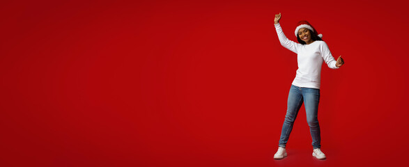 A joyful individual wearing a Santa hat and casual clothing dances energetically in front of a...