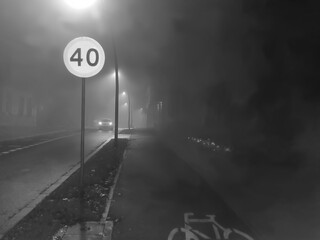 Mglista ulica miejska w Ostrowcu Świętokrzyskim w Polsce, uchwycona nocą w podczerwieni. Znak ograniczenia prędkości do 40 km/h i latarnie oświetlają drogę. Zdjęcie ma niepokojący, eteryczny charakter © Grzegorz