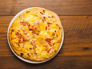 German pizza style dish with ham, potato, cheese and creamy sauce on a wooden table. Popular and tasty dish. Simple dinner.