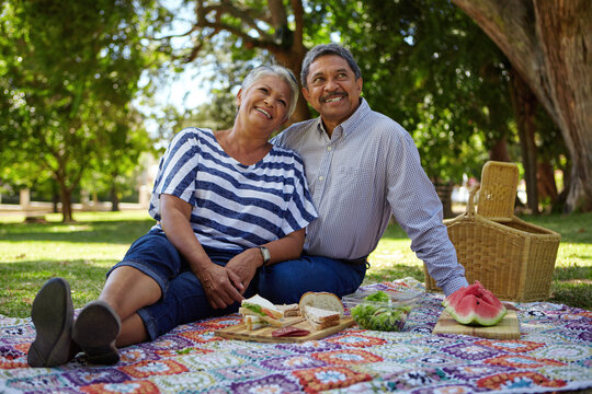 Happy, senior couple and picnic outdoor with love, romantic date and bonding together. Smile, elderly people and rest with food for anniversary, sightseeing and partner affection on holiday at park - Powered by Adobe