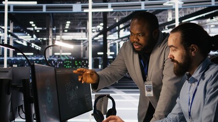 Server farm manager overseeing engineer examining neural network algorithms. Data center team leader and worker reviewing performance dashboards of artificial intelligence infrastructure, camera A