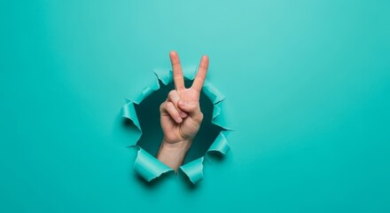 Hand showing peace sign through ripped turquoise paper hole