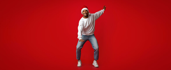 A man wearing a festive sweater and Santa hat dances happily against a vibrant red background. His joyful expression captures the spirit of celebration and holiday cheer.