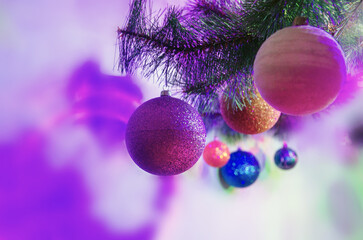 Colorful Christmas decorations hanging on a Christmas tree branch with bright purple and pink holiday lights. Background with shiny balls, and bright bokeh, Christmas and New Year background with ball