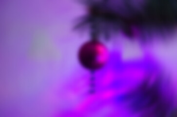 Soft blurred Christmas background with colorful holiday decorations and glowing purple lights. New Year background, backdrop with blurred ball hanging on a Christmas tree branch.