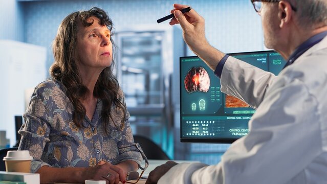 Male doctor performing a neurological examination with a pen light to assess a patient cognition, pupil response and reflexes, checking for signs of concussion or brain injury. Camera B.