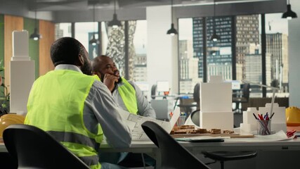Property developers and architects in meeting reviewing blueprints and structural designs for zoning regulations. Team discusses project approval and city planning for housing growth. Camera B.