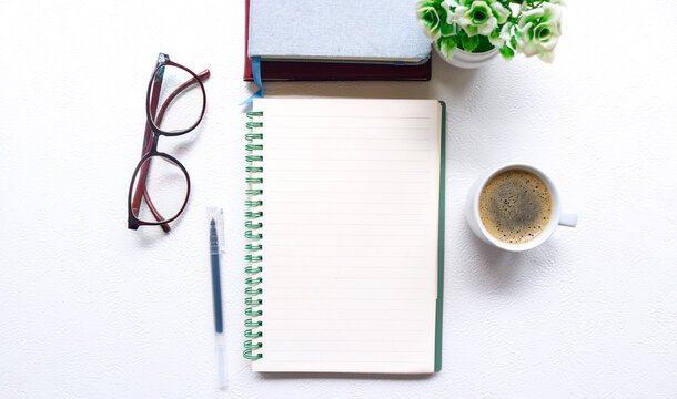 Blank notebook for text on white office desk table with books, pen, glasses, clock and other. Blank notebook page for input the text in the middle. Top view, flat lay.