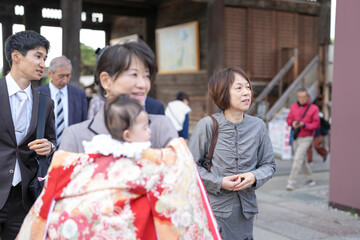 A woman is holding a baby in a red and white kimono. She is smiling at the baby