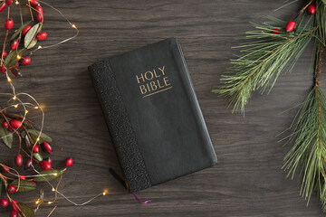 Christian bible with border of evergreen and red berries with Christmas lights