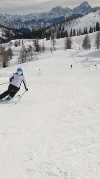 Experienced female skier carving down the groomed slope of a snowy alpine ski resort. Unrecognizable woman enjoys skiing during an active winter vacation in the beautiful mountains of Austrian Alps.