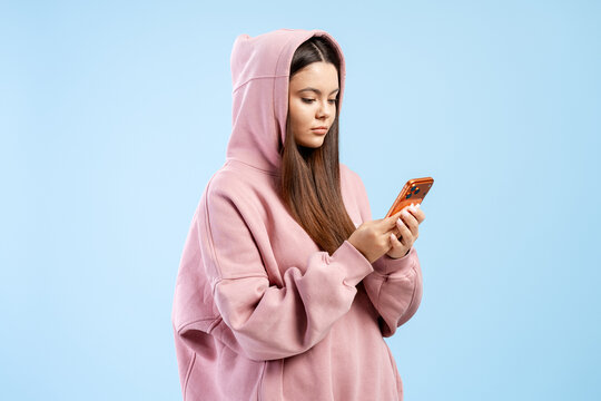 Young woman in pink hoodie sending messages using a smartphone on a blue background