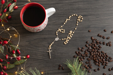 Coffee and rosary prayer beads with a Christmas border on dark wood