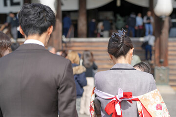 A man and a woman are standing in front of a building. The man is wearing a suit and tie, while the...