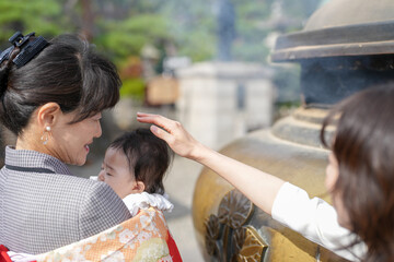 A woman is holding a baby in a red and white blanket. The baby is wearing a white outfit. The scene...