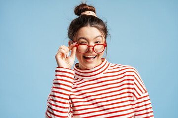 Young woman winking, smiling, playing with glasses, having fun on a blue background