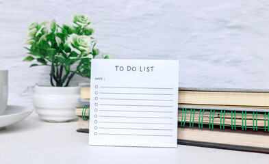 To do list sheet on desk surrounded by books, glasses, clock, coffee. Checklist of tasks to complete. Business planning, design and reminder. To do list and list of numbers on a table.