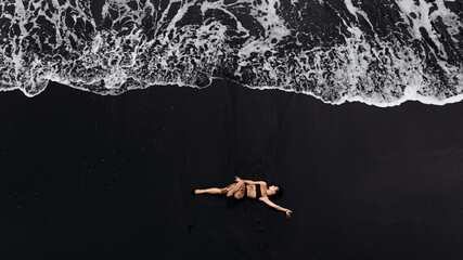 Woman relaxing on a black sand beach, surrounded by gentle waves, enjoying the serene atmosphere, embodying tranquility and connection with nature in a peaceful moment