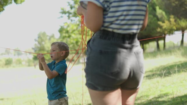 Little boy helping his mother untangle a string in the park
