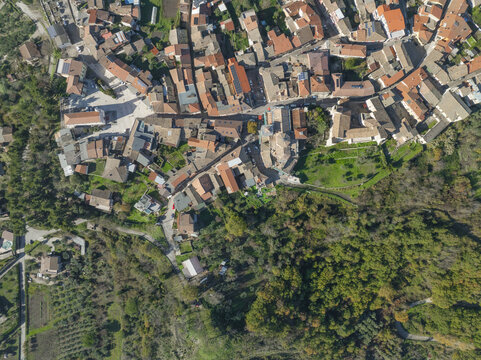 Aerial view of sun-kissed rooftops cascading down the hillside, a tapestry of terracotta and umber amidst the vibrant green foliage, Lapio, Irpinia, Campania, Italy.