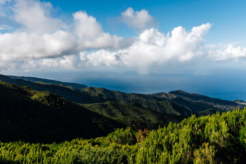 Lush green mountains stretch towards the horizon under a bright blue sky with fluffy clouds, creating a serene and picturesque landscape for nature lovers and travelers seeking adventure