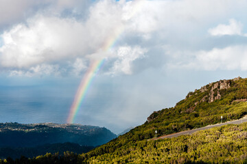 Fototapeta premium Scenic view of a vibrant rainbow arching over lush green hills and a tranquil ocean, creating a picturesque landscape that embodies natural beauty and serenity