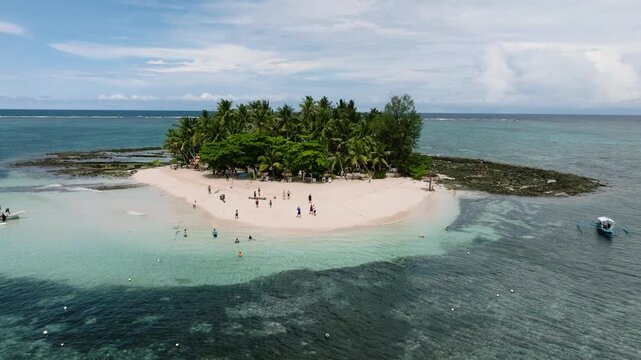 Tourists walk and swim around a small palm covered island with white sand beach. Guyam Island. Siargao, Philippines.