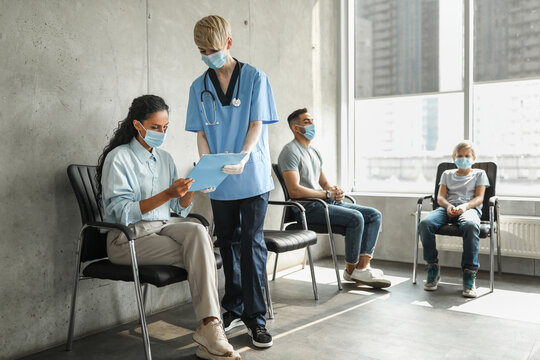 Woman doctor assisting young lady patient with filling medical form before vaccination against coronavirus, international group of people making immunization at clinic, wearing face masks - Powered by Adobe