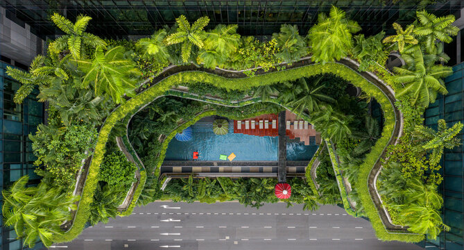Aerial view of lush greenery cascades over the hotel's terraced balconies and pool, contrasting with the grey city street below, Singapore, Central Singapore Community Deve, Singapore.