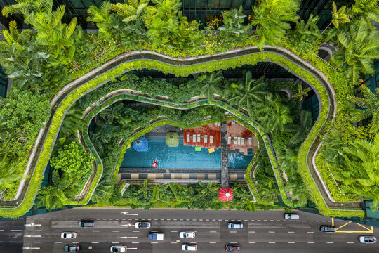 Aerial view of the vibrant green foliage cascading over a hotel with a pool, contrasting with the busy street below, Singapore, Central Singapore Community Deve, Singapore.