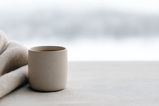 winter self-care, cozy winter self-care morning person wrapping in blanket with herbal tea by frosty window, minimal natural colors, hygge vibes